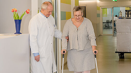 Chefarzt Dr. Hauger hilft Patientin nach Hüftoperation Chefarzt Dr. Hauger hilft Patientin nach Hüftoperation